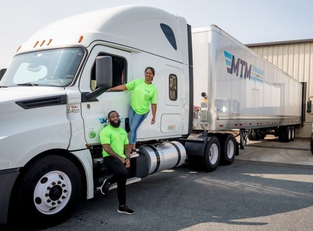 Two MTM Trucking employees posing outside of their truck